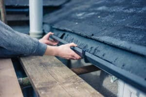 A man performing exterior cleaning and fixing a gutter on a roof.