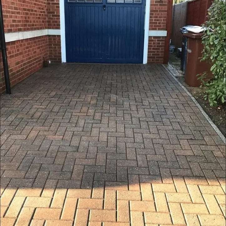 A brick driveway with a blue garage door undergoes exterior cleaning.