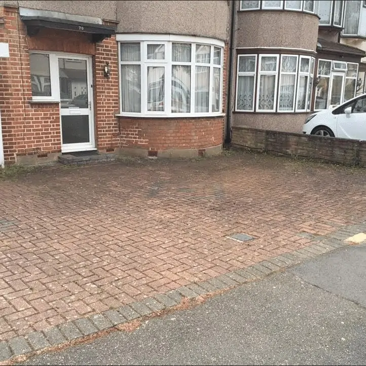 A brick driveway with a car parked in front of it, undergoing exterior cleaning.