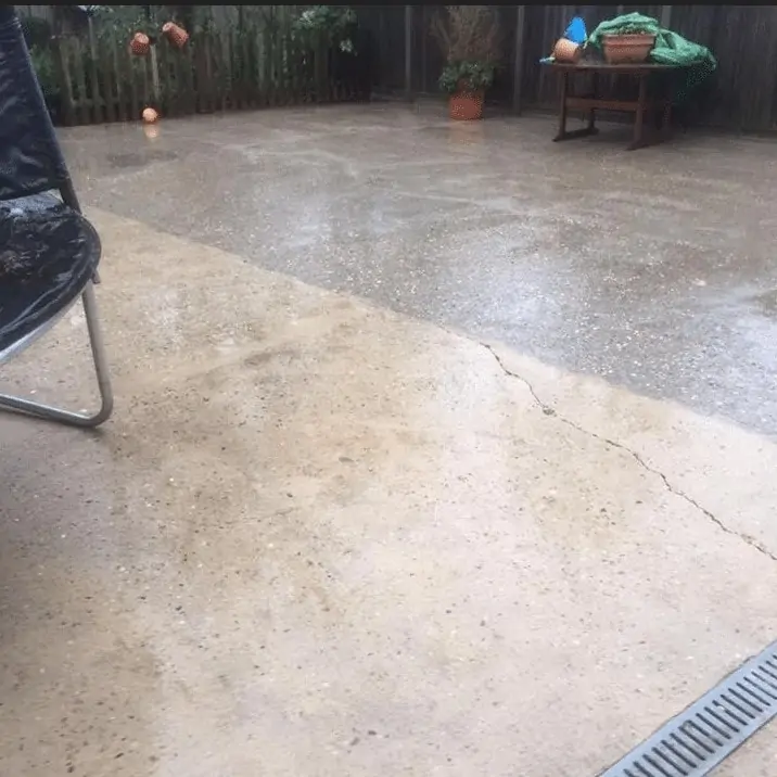 A concrete patio with a table and chairs undergoing exterior cleaning.