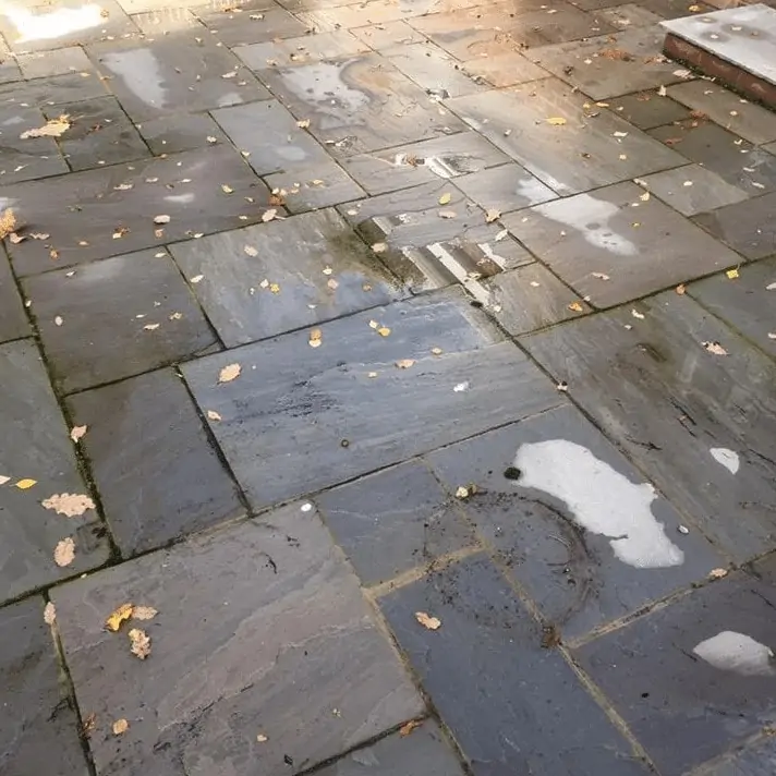 A stone patio with leaves on it, in need of exterior cleaning