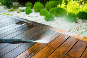 A man using a pressure washer for exterior cleaning of a wooden deck.