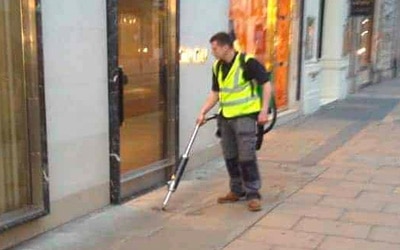 A man performing exterior cleaning of a store sidewalk.